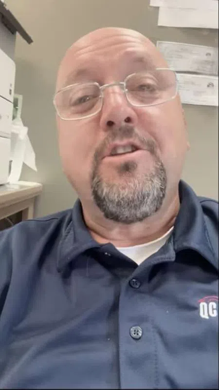 Middle-aged man with glasses and goatee wearing a navy blue shirt in an office setting.