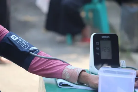 Person's arm with blood pressure cuff connected to Omron digital monitor showing reading 129 outdoors.
