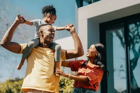 Happy family outdoors with father carrying daughter on shoulders and mother smiling beside them