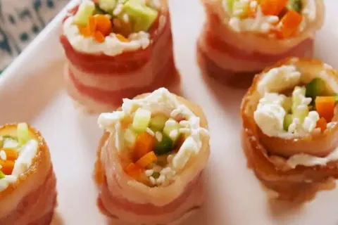 Bacon rolls filled with cream cheese, cucumber, carrot, and rice on a white plate.