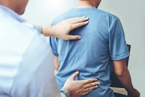 Therapist performing physical therapy by examining patient's back and lower spine.