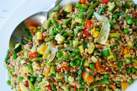 Colorful vegetable and grain salad with peas, asparagus, zucchini, peppers, and grains in a bowl with a spoon.