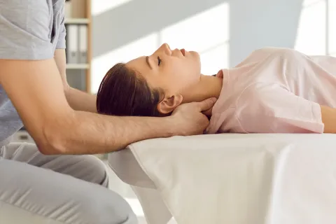 Therapist performing neck massage on a woman lying relaxed on a treatment table.