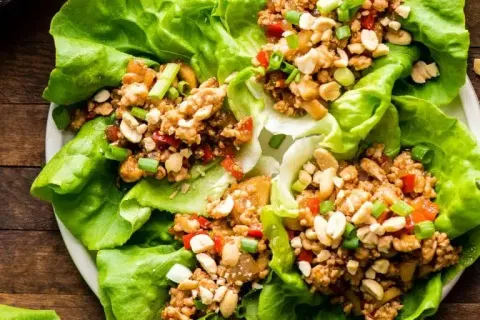 Fresh lettuce wraps filled with seasoned ground meat, chopped peanuts, red peppers, and green onions on a white plate.