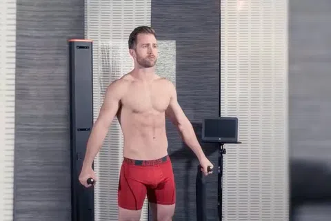 Man in red shorts using fitness equipment in a modern indoor gym with grey walls and digital screens.
