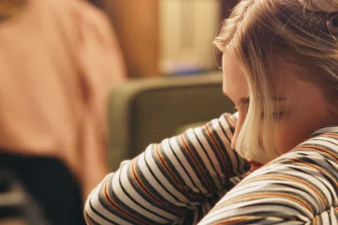 Young woman resting her head on crossed arms wearing a striped shirt in a cozy indoor setting.