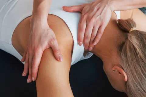 Therapist performing shoulder massage on woman lying face down on a treatment table