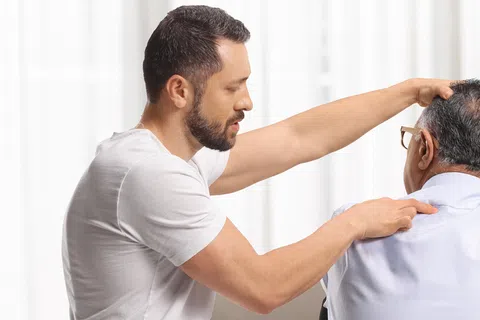 Young male chiropractor examining elderly man's neck during a therapy session in a bright home setting