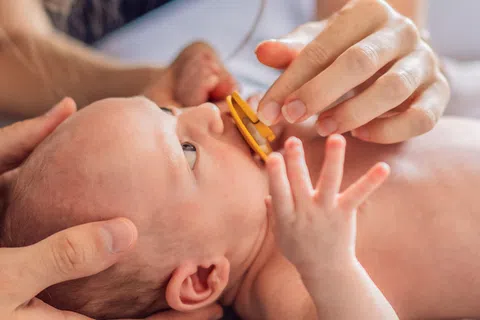 Newborn baby lying down while parents gently hold and feed with a pacifier at home.