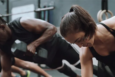 People performing dumbbell renegade rows in a gym with focused expressions and athletic attire.