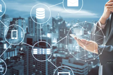 Businessman holding phone with digital technology icons and city skyline in background representing connectivity.