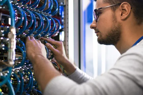 Technician with glasses working on complex server cables and hardware inside a data center rack.