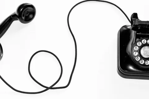 Black vintage rotary dial telephone with handset off the base and cord extended on white background