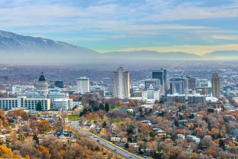 Aerial view of Salt Lake City downtown with autumn trees, buildings, and mountains under a cloudy sky.
