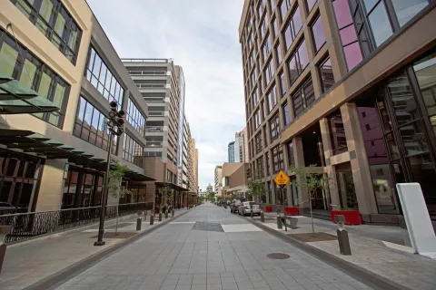 Empty urban street flanked by modern glass office buildings under a cloudy sky.