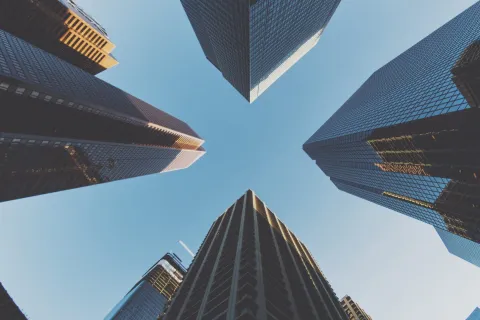 View looking up at tall modern skyscrapers with glass facades against a clear blue sky.
