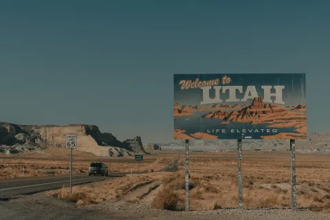 Welcome to Utah sign on desert highway with rocky cliffs under clear blue sky highlights natural landscape.