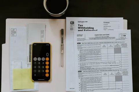 Flat lay of tax forms, smartphone calculator app, pen, envelopes, and a cup of coffee on dark surface