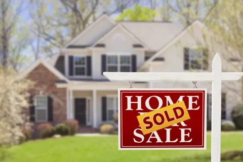 Red and white home sale sign with sold sticker in front of a two-story suburban house with green lawn.