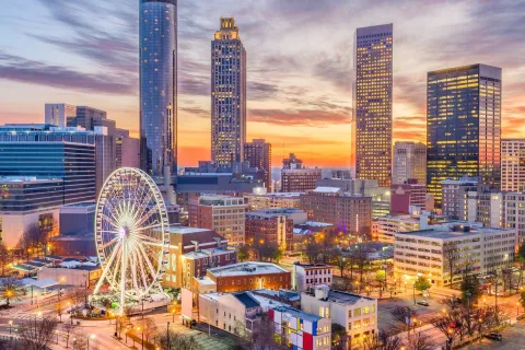 Atlanta city skyline at sunset with tall buildings and a brightly lit Ferris wheel in the foreground