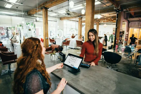 Customer making a payment at the reception of a modern, bright hair salon with wooden accents and styling chairs.