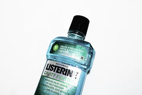 Bottle of blue Listerine cavity fighting mouthwash against a white background with water droplets on the bottle.