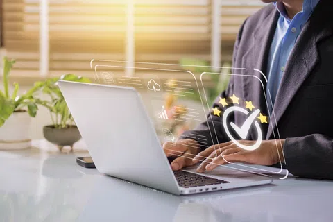 Person working on laptop with digital five-star rating and checkmark overlay, indicating quality or approval.