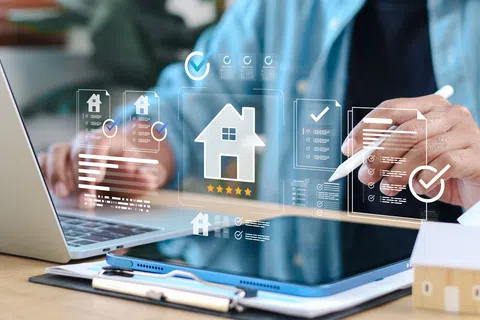 Person using digital tablet and laptop with virtual home icons for real estate or property management.