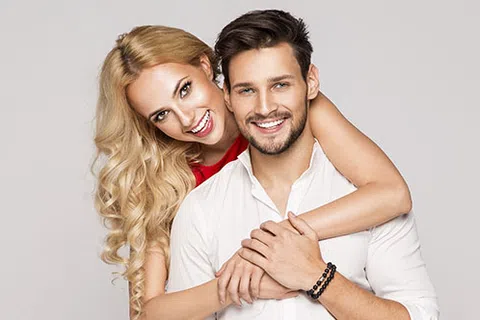 Happy young couple smiling, embracing each other against a neutral background, showing affection and joy.