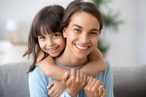 Smiling mother and daughter hugging in cozy home environment, showing love and happiness together.