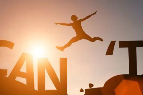 Silhouette of a person leaping over the gap between 'CAN' and 'T' with sunlight in the background.