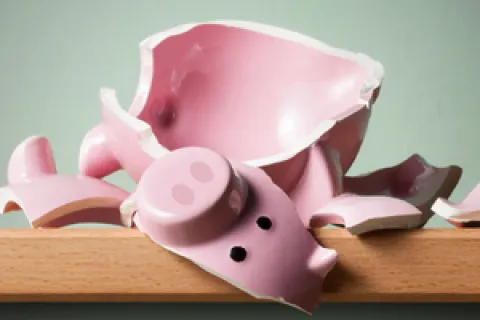 Broken pink piggy bank pieces scattered on wooden surface against gray background symbolizing financial loss