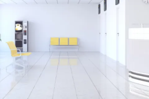 Bright hospital waiting room with yellow chairs, large windows, reception desk, and vending machine.