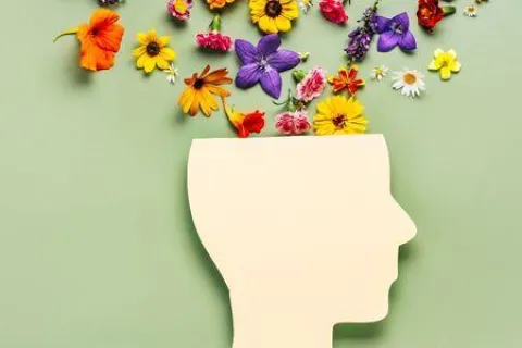 Cutout of a human head with colorful flowers blooming from the top on a green background.