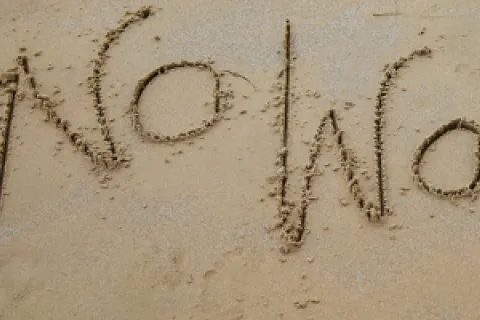 No worries written in sand near the ocean shore with a wave approaching the text.