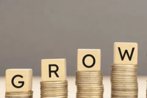 Wooden blocks spelling GROWTH atop increasing stacks of gold coins on a neutral background.