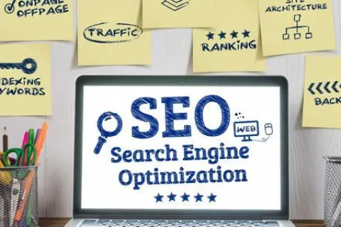 Laptop displaying SEO Search Engine Optimization surrounded by sticky notes with marketing keywords and office supplies.