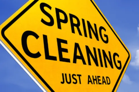 Yellow road sign reading Spring Cleaning Just Ahead against a blue sky with clouds.
