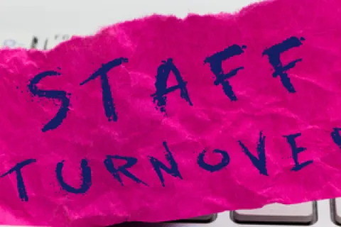 Crumpled pink paper with STAFF TURNOVER text placed on a white computer keyboard symbolizing employee turnover.