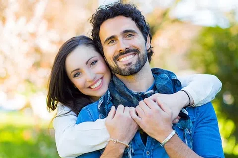 Happy young couple smiling and embracing outdoors with a blurred natural background in daylight.