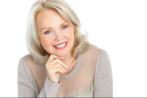 Smiling mature woman with blonde hair wearing beige sweater posing against white background