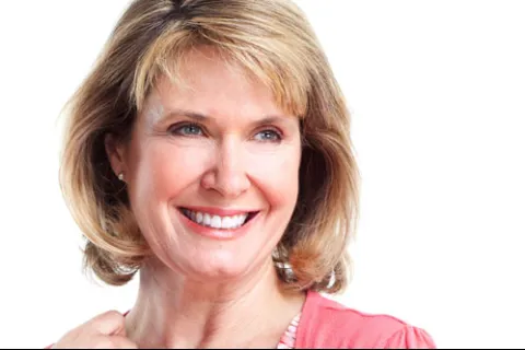 Smiling middle-aged woman with blonde hair wearing a coral top against a white background