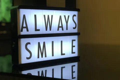 Illuminated sign reading 'ALWAYS SMILE' on a dark surface with a reflective quality.