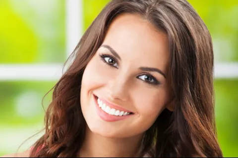Smiling young woman with long hair, bright eyes, and a sunny background, radiating warmth and positivity.