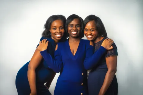 Three smiling women in blue dresses posing together against a plain white background