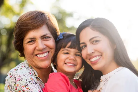 A joyful three-generation family portrait in a sunlit park, showcasing happiness and love.