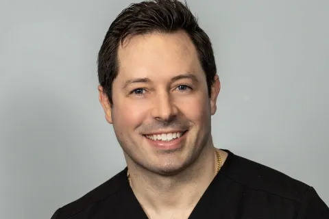 Smiling dentist in black scrubs against a neutral background, showcasing a friendly professional demeanor.