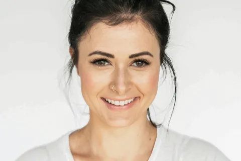 Smiling woman with a top knot hairstyle against a light background, radiating confidence and warmth.