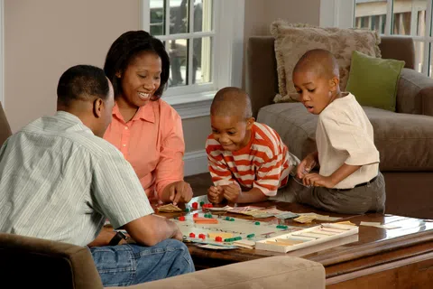 Family of four playing board game together in cozy living room near window and couch