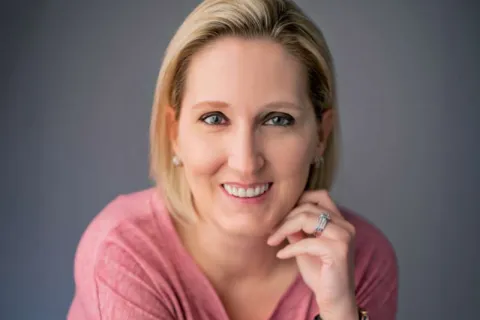 Smiling woman with blonde hair wearing a pink shirt showing white teeth after dental veneers and crowns.